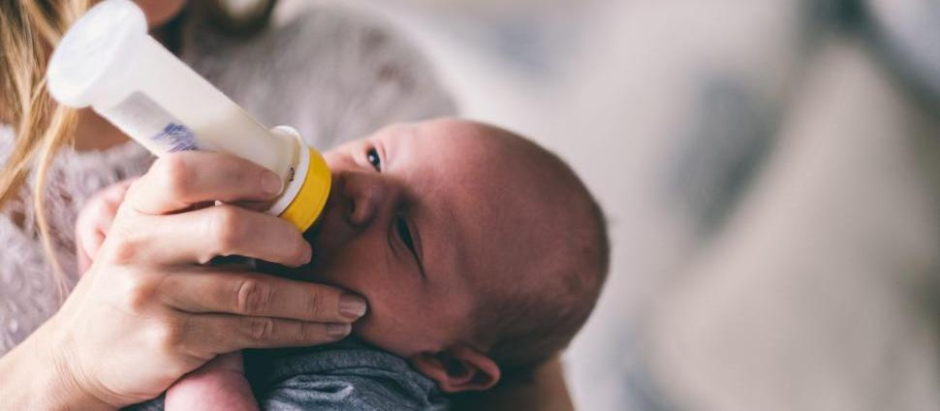 Un bebé bebe leche de un biberón