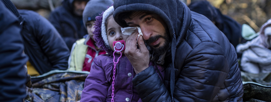 A man holding a child reacts as the members of the Kurdish family from Dohuk in Iraq wait for the border guard patrol, near Narewka, Poland, near the Polish-Belarus border on November 9, 2021. - The three-generation family of 16 members with seven minors, including the youngest who is five months old, spent about 20 days in the forest and was pushed back to Belarus eight times. They claim they were beaten and frightened with dogs by Belarusian soldiers. (Photo by Wojtek RADWANSKI / AFP)
