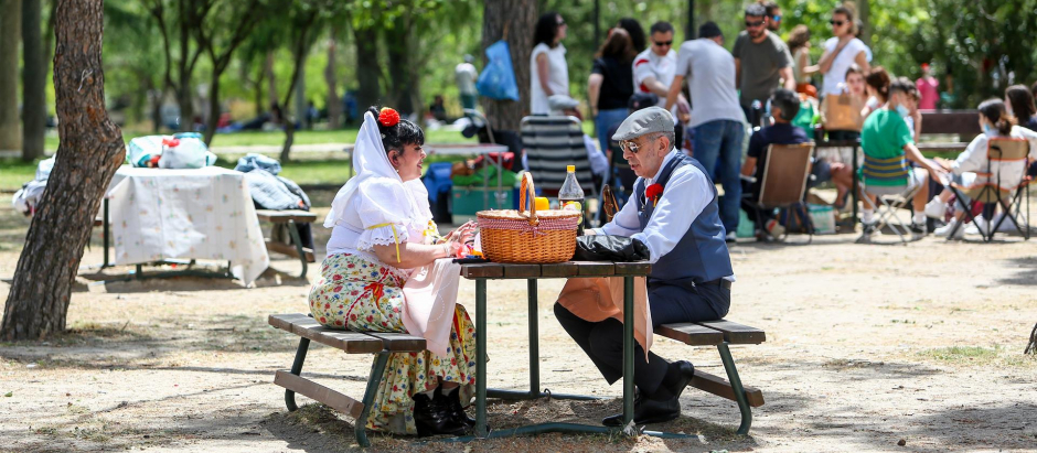 Una pareja vestida con el traje típico madrileño come en una mesa de la pradera de San Isidro, una de las zonas típicas donde se reúne la gente en las fiestas del patrón, a 14 de mayo de 2021, en Madrid
