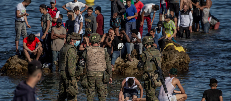 Soldados del Ejército de Tierra observan como un grupo de inmigrantes alcanzan la playa fronteriza de El Tarajal de Ceuta