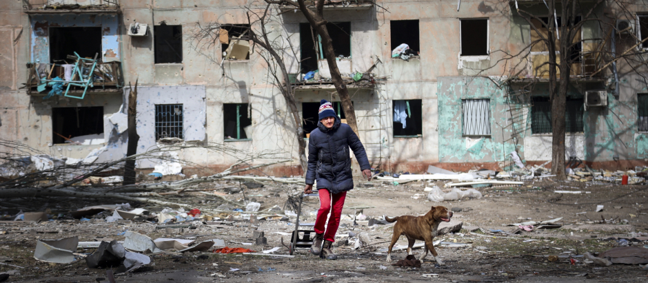 Un hombre camina con su perro frente a un edificio de apartamentos de Mariúpol destrozado por las bombas