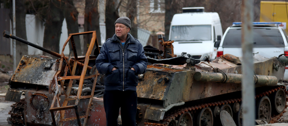 Un hombre camina frente a un tanque destrozado en Bucha, Ucrania