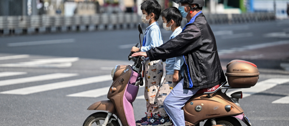 Un hombre conduce una moto con dos niños en Shanghái, este miércoles