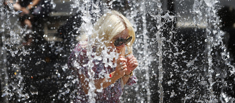 Una turista mitiga el calor en los chorros de una fuente de un parque de Alicante