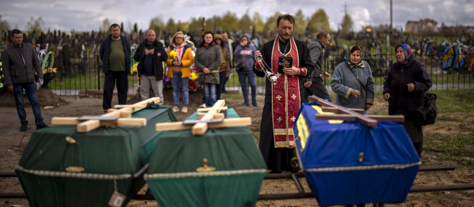 A priest blesses the remains of three people who died during the Russian occupation and were disinterred from temporary burial sites in Bucha, on the outskirts of Kyiv, on Wednesday, April 27, 2022. (AP Photo/Emilio Morenatti)