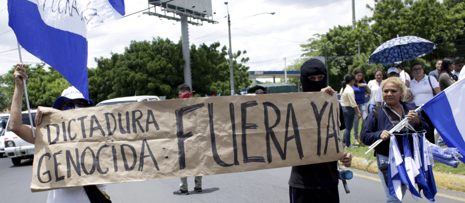 People hold a banner with a message that reads in Spanish: "Genocidal Dictatorship Out Now" during a demonstration supporting journalists recently attacked while covering protests demanding the resignation of President Daniel Ortega and the release of all political prisoners, in Managua, Nicaragua, Monday, July 30, 2018.