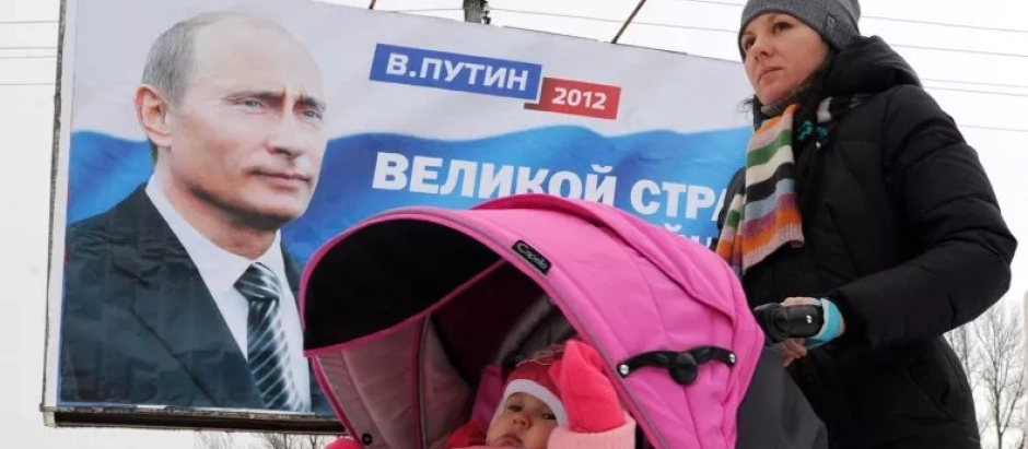 Pancarta de Vladimir Putin de las elecciones de 2012 mientras una madre pasea con su hijo