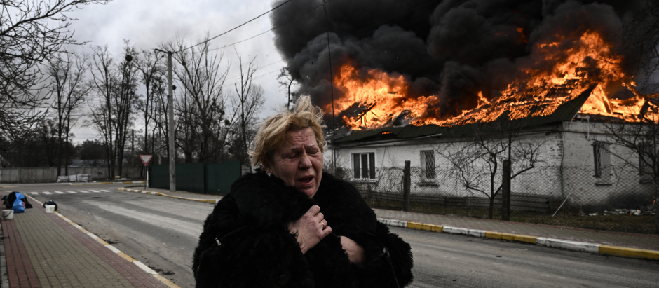 Una mujer frente a una casa en llamas después de ser bombardeada en la ciudad de Irpin