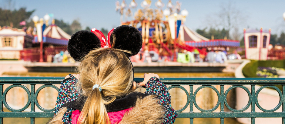 Una niña con orejas de Minnie Mouse ve a lo lejos unas atracciones de Fantasyland, en Disneyland París