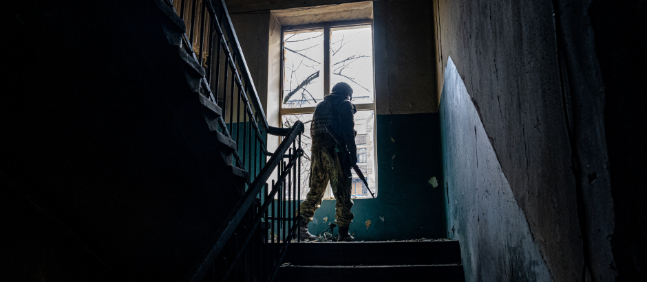 A Ukrainian serviceman looks through a broken window of a damaged residential building as the sounds of shelling continue in Bakhmut on February 27, 2023, amid Russia's military invasion on Ukraine. (Photo by DIMITAR DILKOFF / AFP)