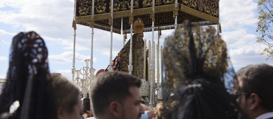 Dos mujeres vestidas de Mantilla ven el paso de la Virgen de la Victoria, en la Semana Santa en Sevilla