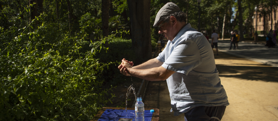 Un hombre se refresca con el agua de una fuente en Sevilla