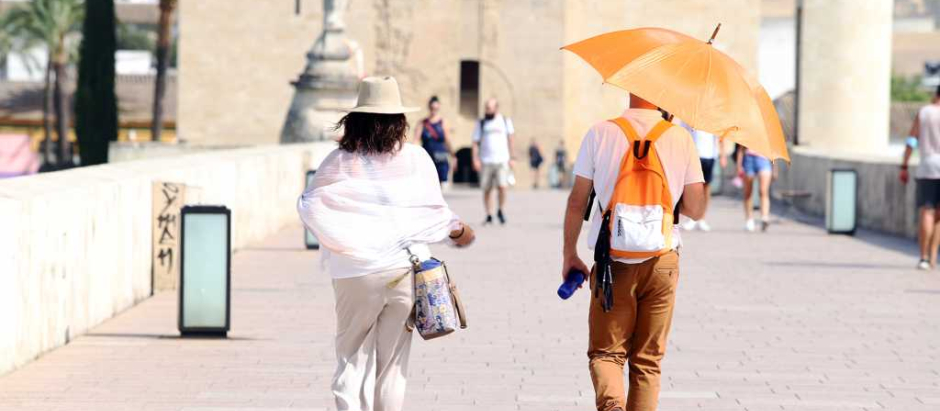 Dos turistas caminan por el Puente Romano de Córdoba en una jornada de calor.
