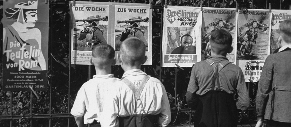Niños alemanes observan el periódico antisemita Der Stürmer y otros carteles de propaganda nazi