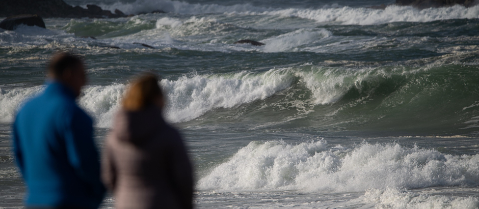Dos personas observan el mar con olas por el temporal, en la playa de A Lanzada