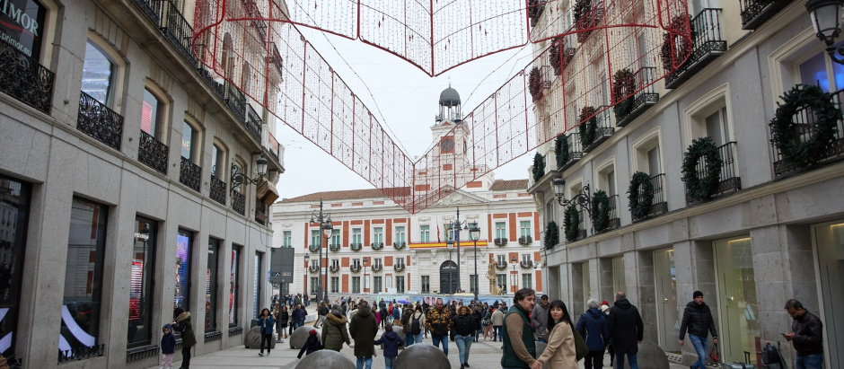 Varias personas en una calle comercial frente a la remodelada y peatonalizada Puerta del Sol