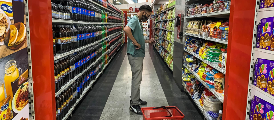 Un hombre revisa su móvil mientras compra comida en un supermercado, hoy, en Caracas (Venezuela)