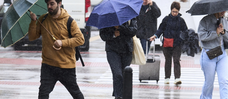 Varias personas se cubren de la lluvia y el viento con paraguas