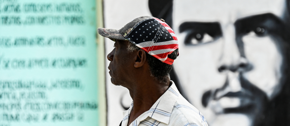 Un hombre con una gorra de EE.UU. camina junto a un letrero con la imagen del Che en La Habana