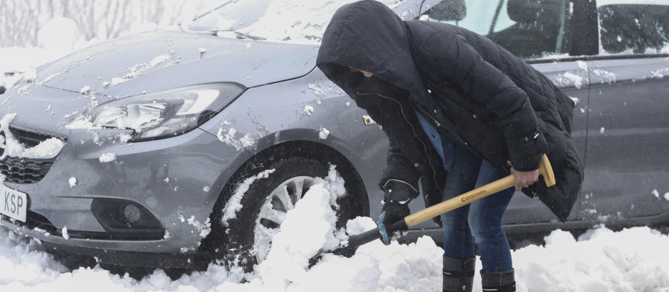 Una mujer trata de despejar la nieve acumulada en la carretera para poder circular con su vehículo este sábado en O Cebreiro, Lugo