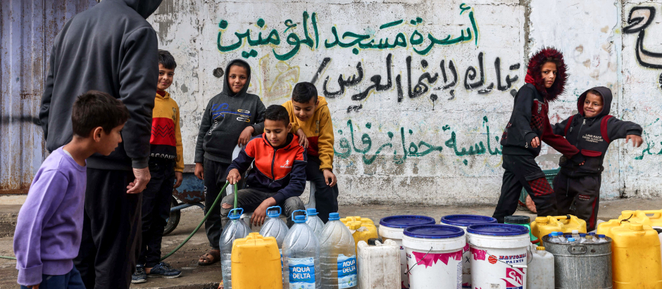 Un niño llena contenedores de agua con una manguera en Rafah, en el sur de la Franja de Gaza