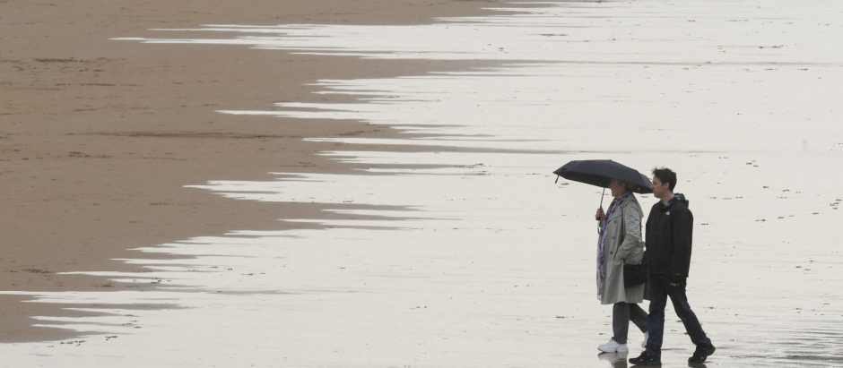 Gente paseando bajo la lluvia en la Playa de San Lorenzo de Gijon