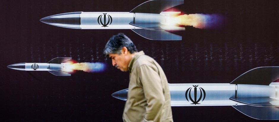 Un hombre pasa junto a una pancarta que representa misiles a lo largo de una calle de Teherán