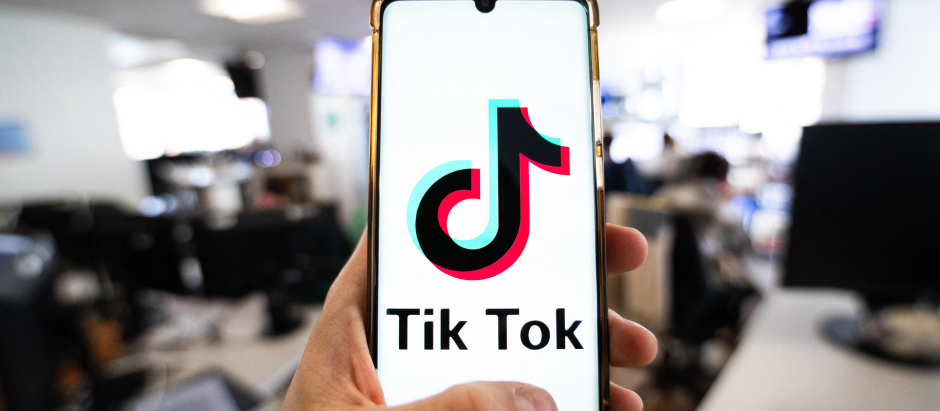 Un hombre sosteniendo un teléfono inteligente con el logotipo de la plataforma china Tiktok en una oficina en París