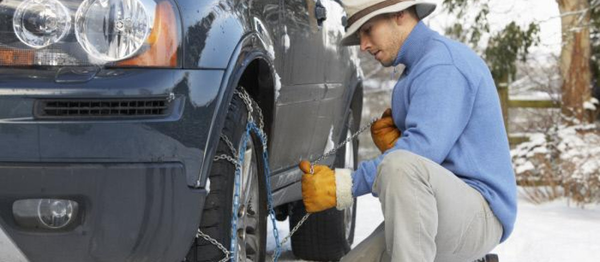 Un hombre instala las cadenas de nieve en su coche