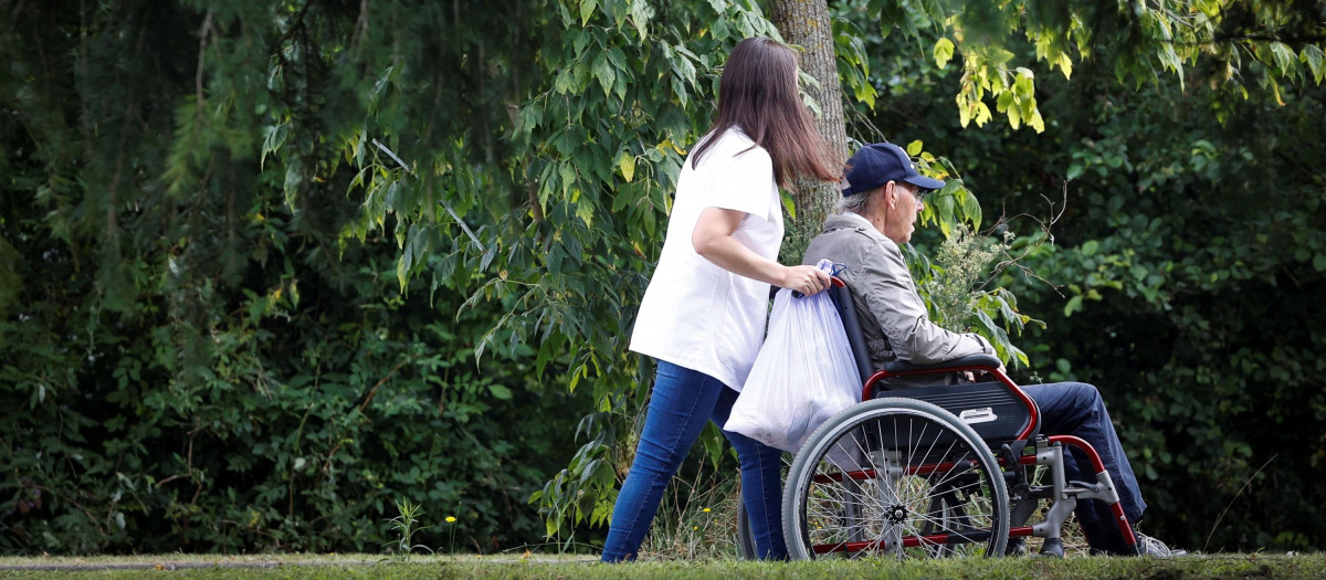Una mujer pasea con un hombre en silla de ruedas junto a una residencia en San Sebastián