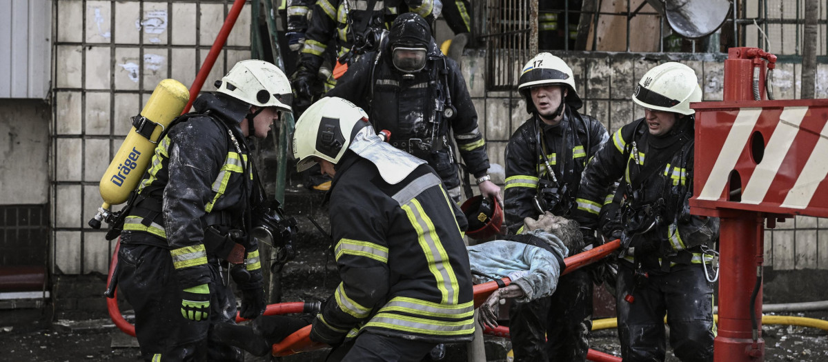 Varios bomberos retiran el cuerpo de una mujer de un edificio de viviendas bombardeado, este martes