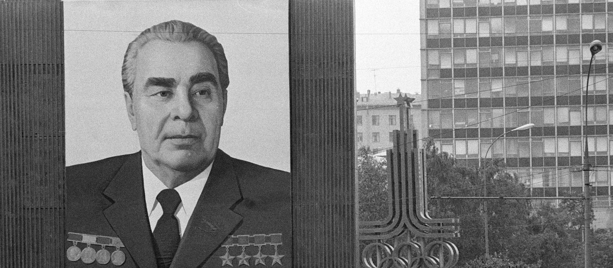 Una mujer pasa junto a un enorme retrato del líder del Partido Comunista, Leonid Brezhnev, que empequeñece el símbolo de los próximos XXII Juegos Olímpicos de Verano, justo detrás, en Moscú