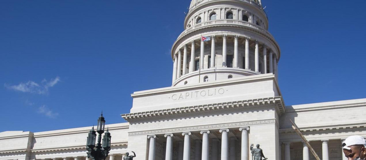 Personas conducen hoy un triciclo cargado con productos agrícolas frente al Capitolio, en La Habana