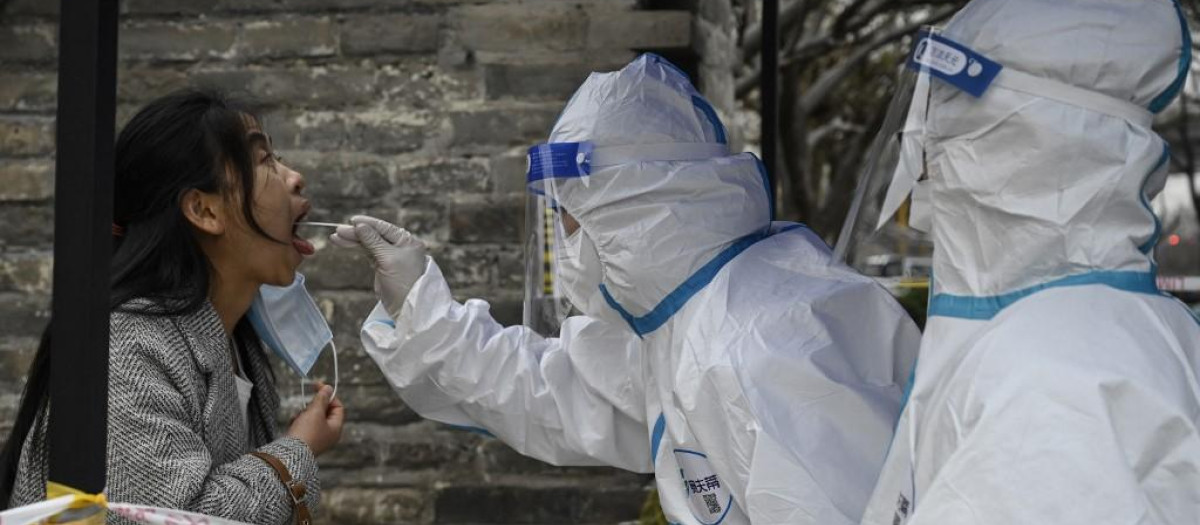 Un sanitario toma una muestra de saliva a una joven en Pekín