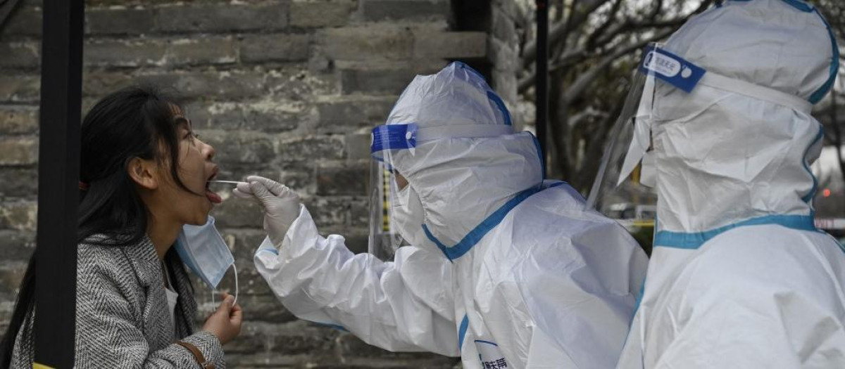 Un sanitario toma una muestra de saliva a una joven en Pekín