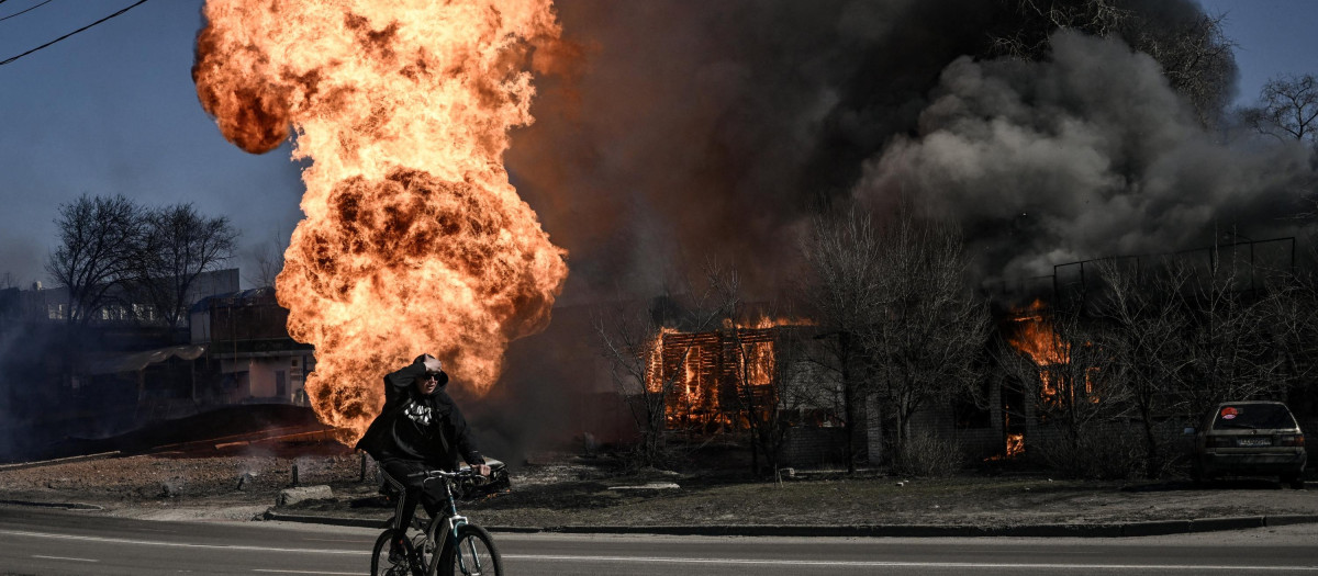 Un ciclista pedalea cerca de las llamas, vestigios de una explosión, en la ciudad ucraniana de Járkov