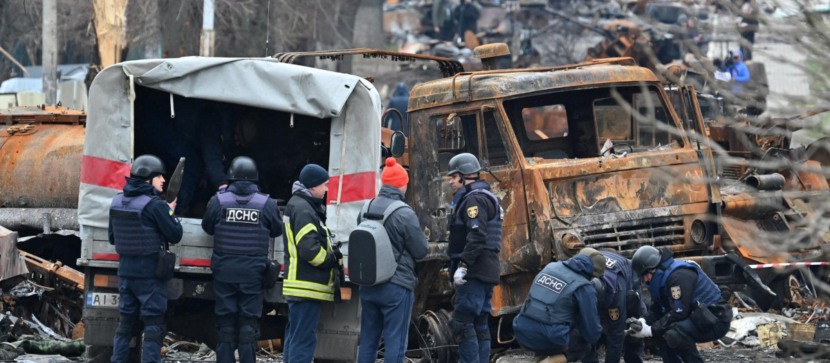 Los ingenieros ucranianos realizan la limpieza de minas entre los vehículos destruidos en una calle de Bucha