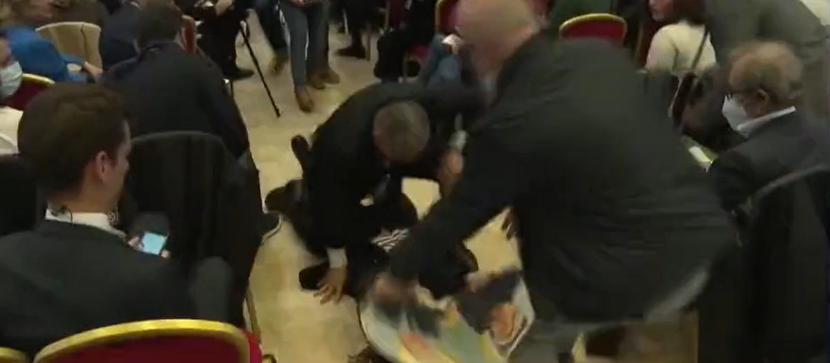 El momento en el que una espontánea es derribada tras enseñar una fotografía de Marine Le Pen con Putin en un acto de la derechista