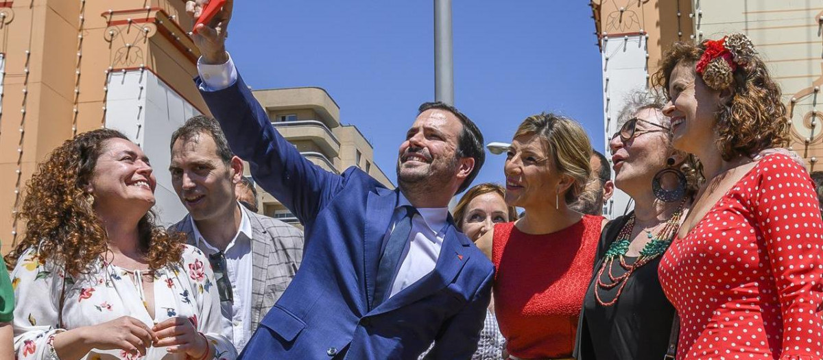 La vicepresidenta segunda del Gobierno y ministra de Trabajo, Yolanda Díaz (3d), y el ministro de Consumo y líder de IU, Alberto Garzón (c), se hacen una fotografía con varias personas junto a la portada de la Feria de Abril de Sevilla