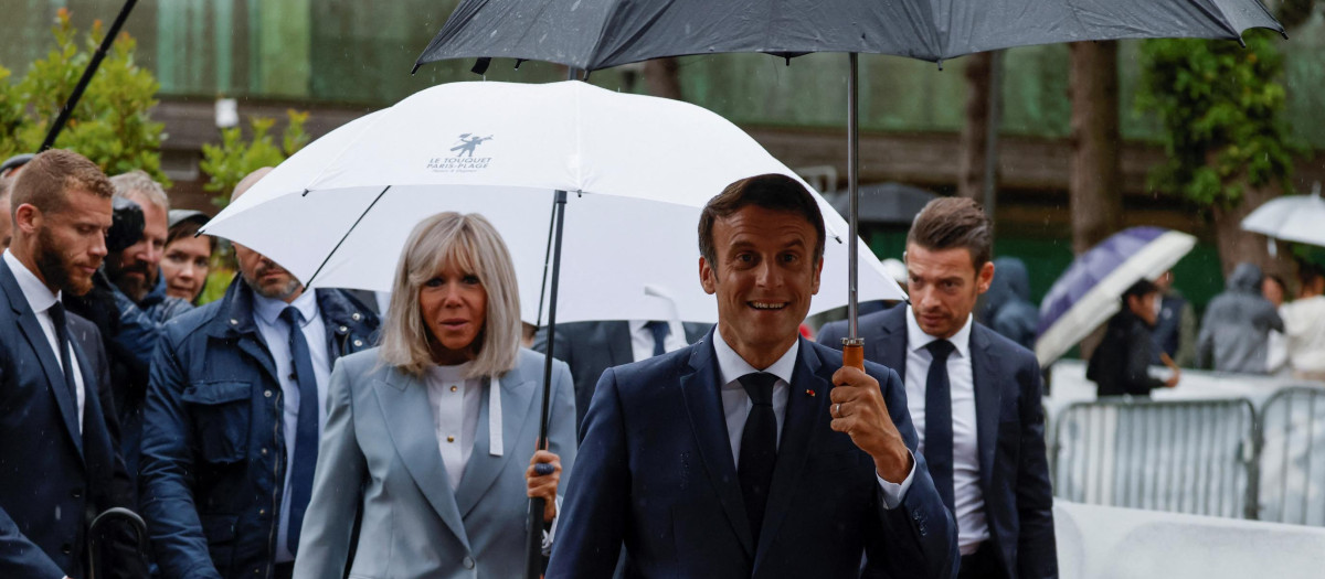 France's President Emmanuel Macron (C) walks with his wife Brigitte Macron (C/L) as he prepares to speak with onlookers as he leaves after casting his vote in the second stage of French parliamentary elections at a polling station in Le Touquet, northern France on June 19, 2022. (Photo by Ludovic MARIN / AFP)