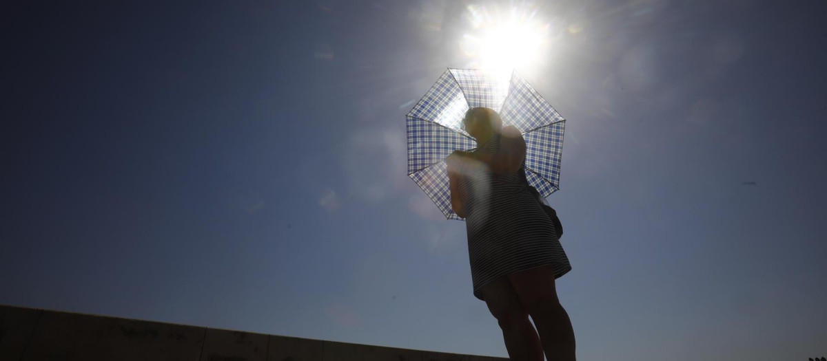 Una mujer se protege del sol con un paraguas mientras pasea por el puente romano de Córdoba, este lunes