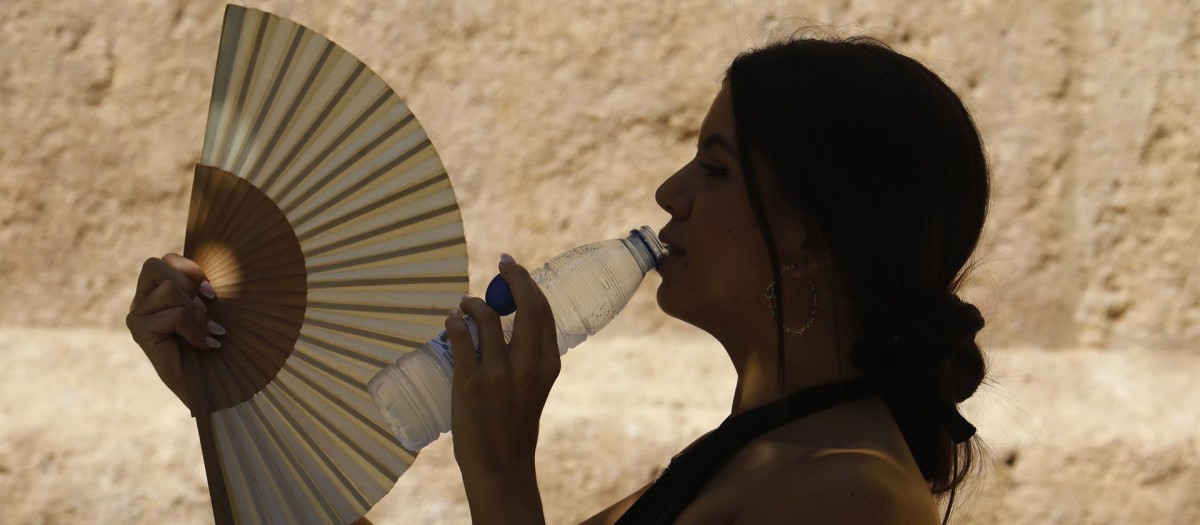 Una mujer bebe agua y se abanica mientras pasea por el barrio de la Judería de Córdoba