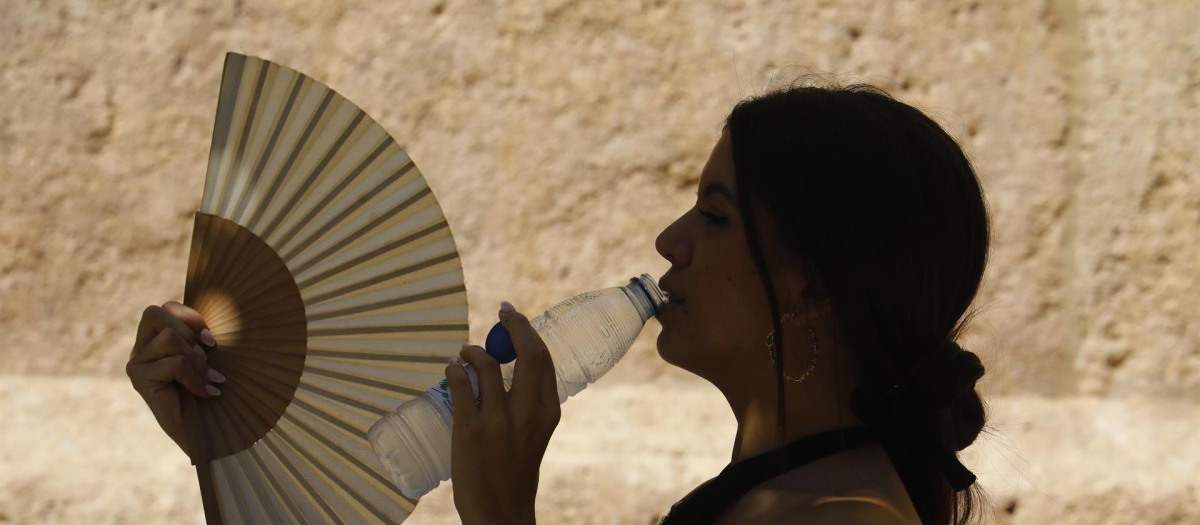 Una mujer bebe agua y se abanica mientras pasea por el barrio de la Judería de Córdoba