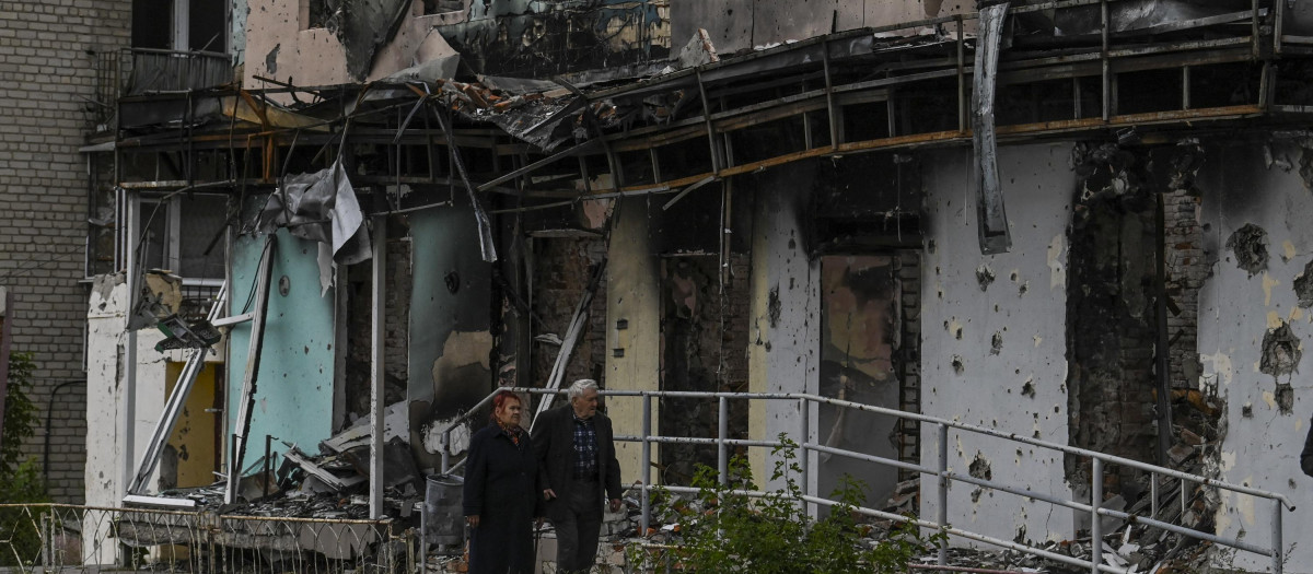 Dos personas caminan frente a un edificio en escombros en Izyum, región de Kharkiv