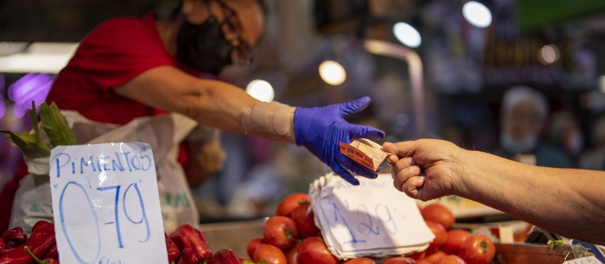 Un cliente paga su compra en un puesto de verdura en el mercado de Maravillas, en Madridfruteria