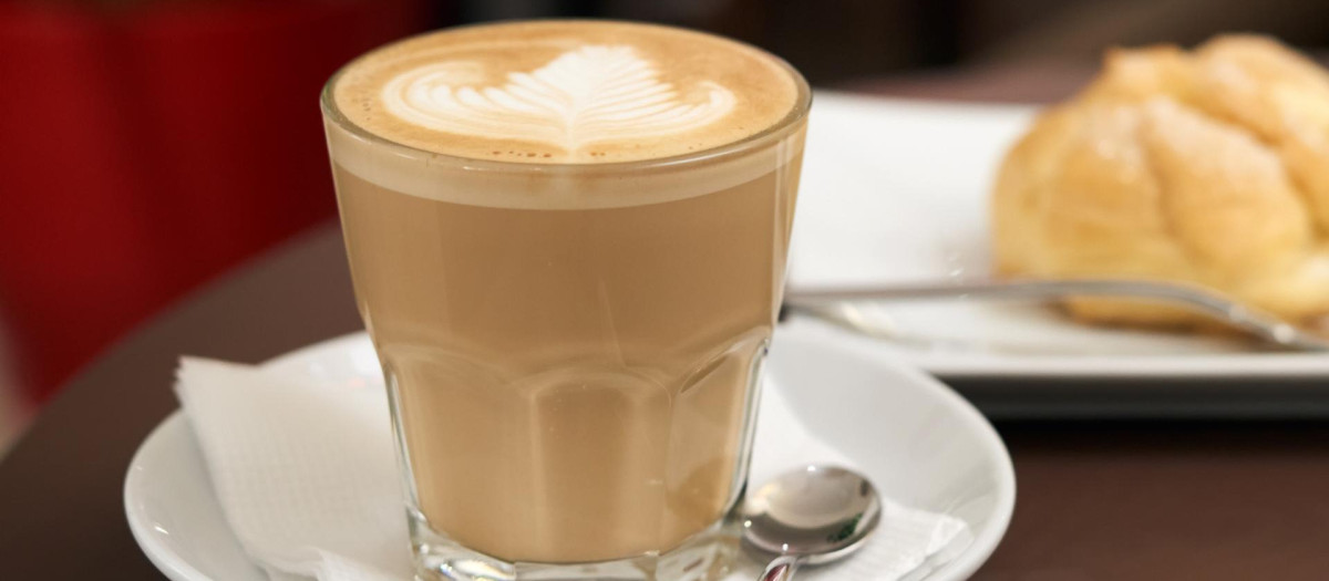flat white coffee in a transparent glass with white foam, behind eclair cake, food on the table in a cafe.white,coffee,in,a,flat,transparent,glass,with,foam,behind,eclair,cake,coffee, white, flat, cup, drink, cafe, food, symbol, black, espresso, table, set, breakfast, beverage, caffeine, cappuccino, morning, restaurant, modern, brown, latte, wooden, office, home, paper, aroma, fresh, break, plate, nobody, liquid, dessert, round, circle, tasty, foam