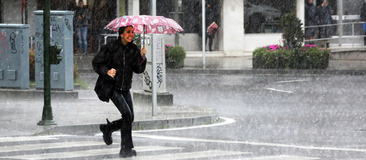 Una mujer pasa por una calle de Compostela, enfrentándose a fuertes lluvias y a un intenso viento