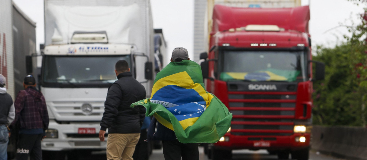 A supporter of President Jair Bolsonaro wears a Brazilian flag during a blockade on Castelo Branco highway, on the outskirts of Sao Paulo, Brazil, on November 2, 2022. - Bolsonarist supporters demonstrated again this Wednesday in Brazil, although the number of roadblocks decreased, after the announcement that Jair Bolsonaro authorized the transition to a new government of Luiz Inácio Lula da Silva. (Photo by Miguel SCHINCARIOL / AFP)