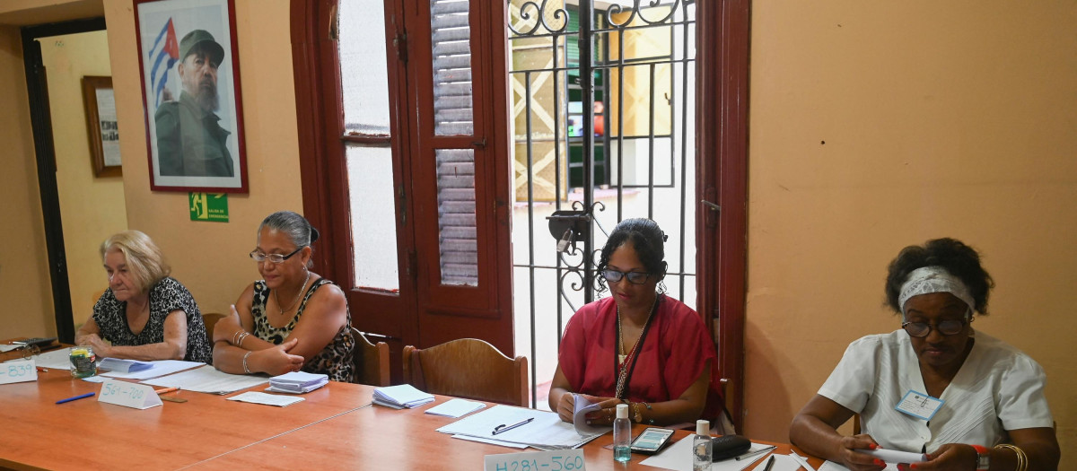 Los miembros de una mesa electoral esperan a los electores de las elecciones municipales bajo el retrato de Fidel Castro