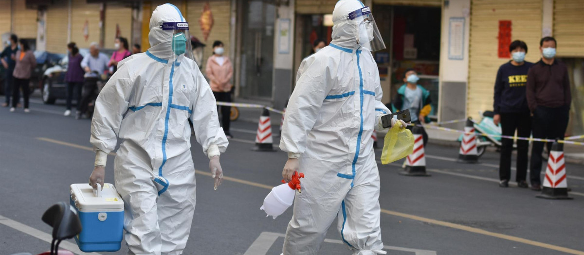 Dos personas con trajes EPI caminan por una ciudad china